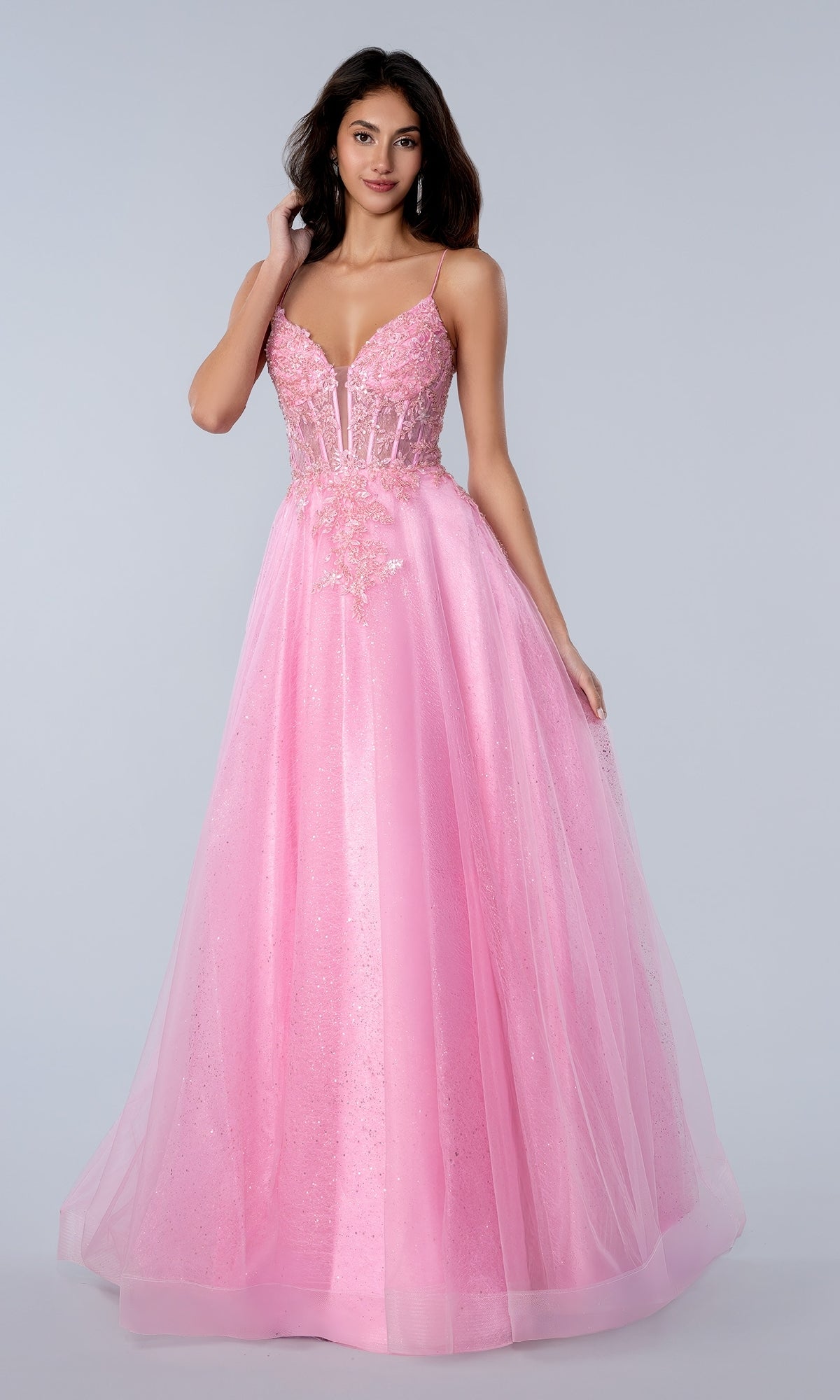 A woman models the Stella Couture 25140 Glitter Prom Ball Gown, featuring a long pink tulle skirt, v-neck corset bodice with thin straps, sequin lace embroidery, and a glitter finish against a plain light background.